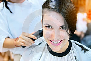 Beauty, hairstyle, treatment and hair care concept - young woman and hairdresser cutting her hair at hairdressing salon.