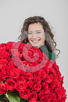 Closeup portrait of a satisfied young woman dressed in green dress holding huge bouquet of roses  over white