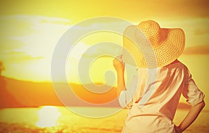 Beauty happy woman in her hat is back and admire sunset over sea