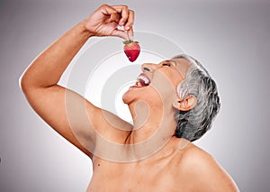 Beauty, health and mature woman with strawberry in a studio eating a diet snack for wellness. Skincare, cosmetic and