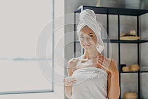 Beauty and hygiene concept. Attractive healthy young woman has shiny perfect smooth skin, applies body cream, holds jar of