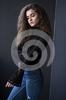 Beauty image of a pretty young woman with curly hair, dressed in a black suitcase and jeans, over grey background.
