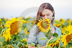 Beauty joyful girl with sunflower enjoying nature and laughing on the field of sunflowers at sunset. Copy space