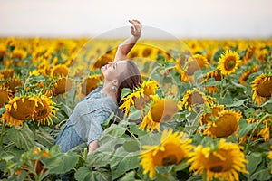 Beauty joyful girl with sunflower enjoying nature and laughing on the field of sunflowers at sunset. Copy space