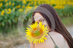 Beauty joyful girl with sunflower enjoying nature and laughing on the field of sunflowers at sunset. Copy space