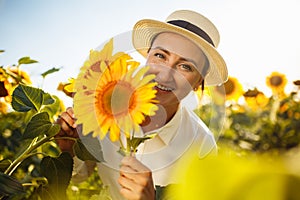 Beauty joyful young woman with sunflowers enjoying nature and laughing on summer sunflower field. Female holding sunflowers.