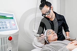 Beauty laser technician performing a cosmetic skin resurfacing session on a female patient, also called a laser peel or photofacia