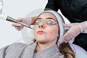 Beauty laser technician performing cosmetic skin resurfacing session on a female patient, also called a laser peel or photofacial