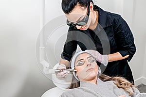 Beauty laser technician performing a cosmetic skin resurfacing session on a female patient, also called a laser peel or photofaciB