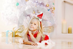 Beauty little Santa girl near the Christmas tree. Happy girl wi