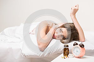 Beauty lying on the bed with a clock and pills