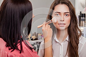 Beauty, make up, cosmetics and people concept - close up of smiling young woman face applying blush with makeup brush