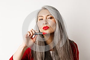 Beauty and makeup concept. Beautiful asian elderly woman pucker lips, showing red lipstick and looking sassy at camera