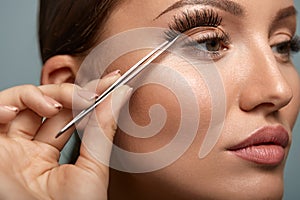 Beauty Makeup. Woman Applying Black False Eyelashes With Tweezer photo