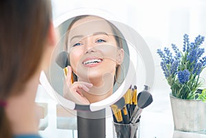 Beauty model girl applying makeup. Beautiful young woman looking in the mirror and applying cosmetic with a big brush