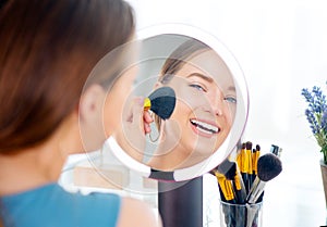 Beauty model girl applying makeup and smiling. Beautiful young woman looking in the mirror and applying cosmetics