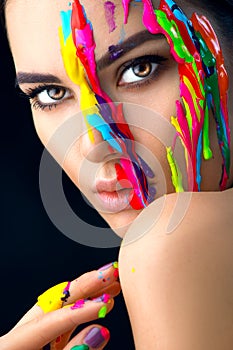 Beauty model girl with colorful paint on her face. Portrait of beautiful woman with flowing liquid paint