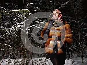 Beauty model girl in night winter forest. beautiful young Woman in fashionable Fur Coat and scarf