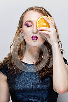 Beauty Model Girl takes Juicy Oranges. Professional make up. Orange Slice holds hand and closes one eye, pouts her lips, eyes clos