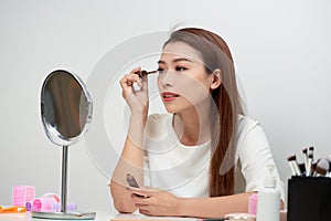 Beauty model teenage girl looking in the mirror and applying mascara make up. Beautiful young woman apply makeup