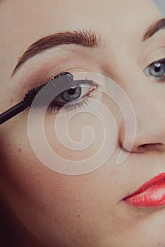 Beauty model teenage girl looking in the mirror and applying mascara make up. Beautiful young woman apply makeup