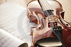 Beauty of musical instruments. Close up view of brown violin lying on sheets with music notes on wooden floor. Violin