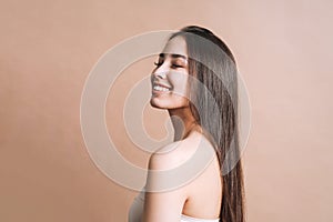 Beauty nude portrait of happy young beautiful asian woman with healthy dark long hair in top bando on beige background