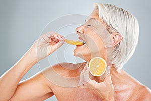 Beauty, orange and eating with a mature woman biting into a fruit slice in studio on a gray background. Food, wellness