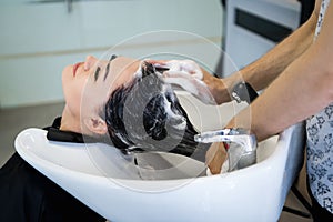 Beauty and people concept - happy young woman with hairdresser washing head at hair salon