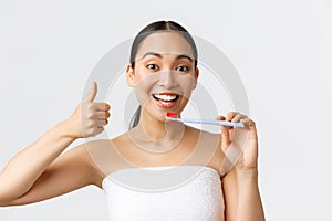 Beauty, personal care, and hygiene concept. Pleased attractive asian woman in bath towel trying new toothbrush, showing