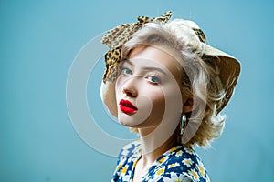 Beauty pin up girl on blue wall. Young woman dressed in pin-up style. Blond model in retro hat posing on isolated grey