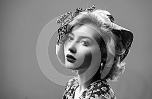 Beauty pin up girl on blue wall. Young woman dressed in pin-up style. Blond model in retro hat posing on isolated grey