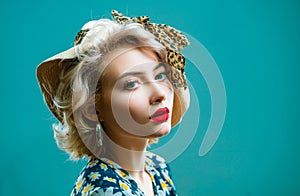 Beauty pin up girl on blue wall. Young woman dressed in pin-up style. Blond model in retro hat posing on isolated grey