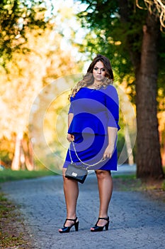Beauty plus size model in blue dress outdoors, fat woman in autumn park among yellow leaves