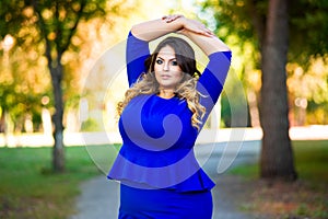 Beauty plus size model in blue dress outdoors, fat woman in autumn park among yellow leaves