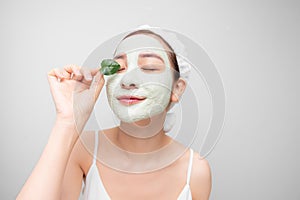 Beauty portrait of Asain woman in towel on head with white nourishing mask on face and green leaf in hand