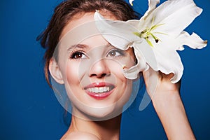 Beauty portrait of attractive, fresh woman with the lily flower on blue