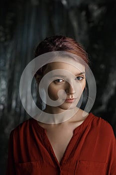 Attractive caucasian girl in red shirt with deep neckline and open clavicles standing against blurred fabric background