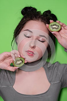 Beauty portrait of attractive young woman with clean radiant skin face with kiwi halves, brunette girl with bare