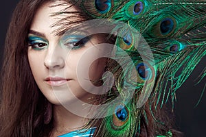 Beauty portrait of beautiful girl covering the eyes with peacock feather. Creative makeup peafowl feathers. Attractive