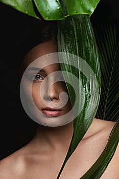 Beauty Portrait of brunette girl in palm leaves. Beautiful young woman with Make-up