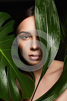 Beauty Portrait of brunette girl in palm leaves. Beautiful young woman with Make-up