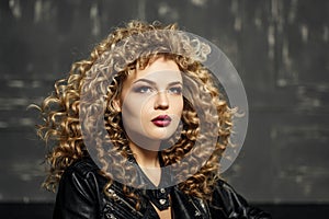 Beauty portrait of curled hair blonde girl in black leather jacket. studio with dark background