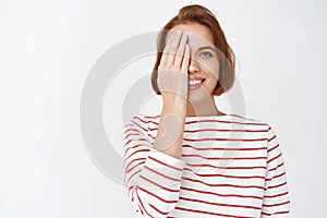 Beauty. Portrait of cute smiling woman cover half face with hand and looking happy, showing before after cosmetics skin
