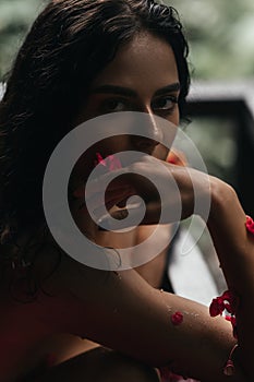 Beauty portrait, face of a young woman in a bath with water and floating red rose petals and rosebuds.