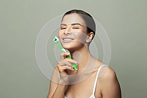 Beauty portrait of a happy attractive woman brushing her teeth with a toothbrush, looking at camera and smiling on white