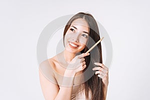 Beauty portrait of happy smiling asian woman with dark long hair combing wooden comb on white background isolated