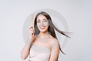 Beauty portrait of happy smiling asian woman with dark long hair combing wooden comb on white background isolated