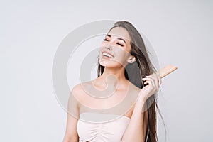 Beauty portrait of happy smiling asian woman with dark long hair combing wooden comb on white background isolated