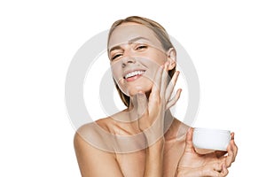 Beauty portrait of happy smiling beautiful half naked girl applying face cream and looking at camera isolated over white